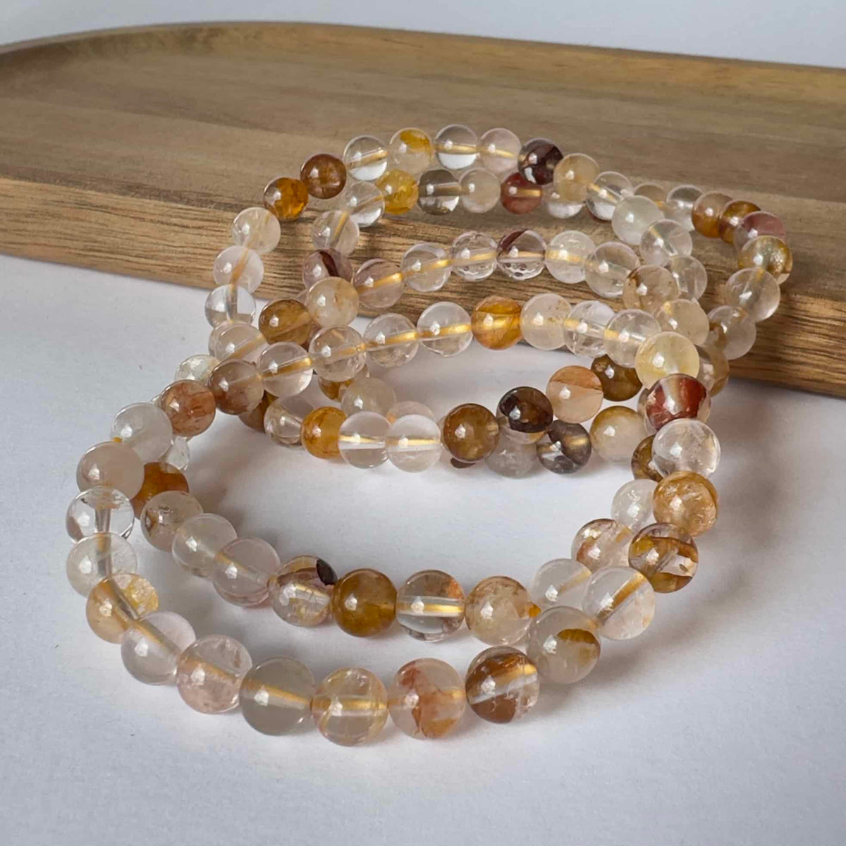 Armbånd lavet af Golden Healer krystalperler, placeret på en træbakke.