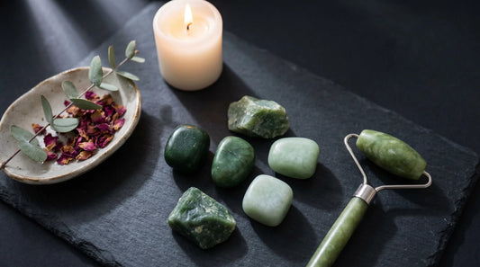 Jade krystaller, jade roller og tændt stearinlys på mørk skifer — dagligt wellness-ritual med jade fra Krystalriget