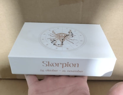 Boks med stjernetegnet Skorpionen på forsiden, datoer 24. oktober - 22. november, holdt i en hånd.