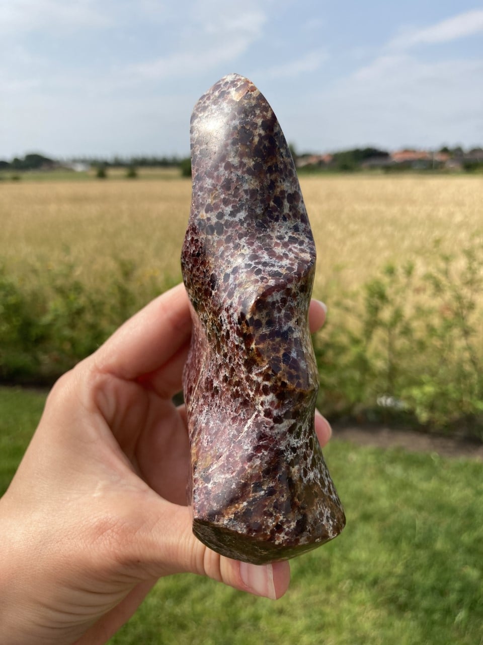 En hånd holder en poleret granat flamme sten foran en mark i dagslys.