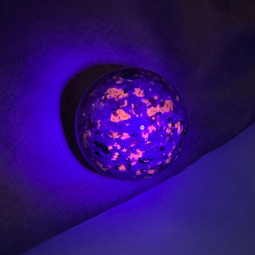 Yooperlit kugle under UV-lys, der afslører lysende mønstre på en mørk baggrund.