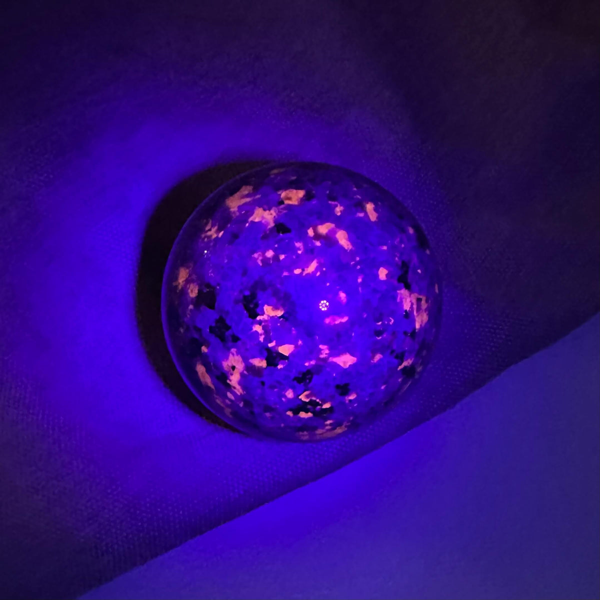 Yooperlit kugle under UV-lys, der fremhæver fluorescerende mønstre i lilla og orange nuancer.