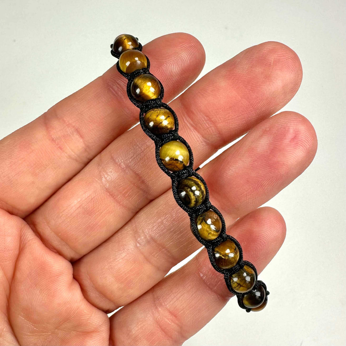 Tigerøje armbånd med brunlige perler holdes mellem fingrene på en lys baggrund.