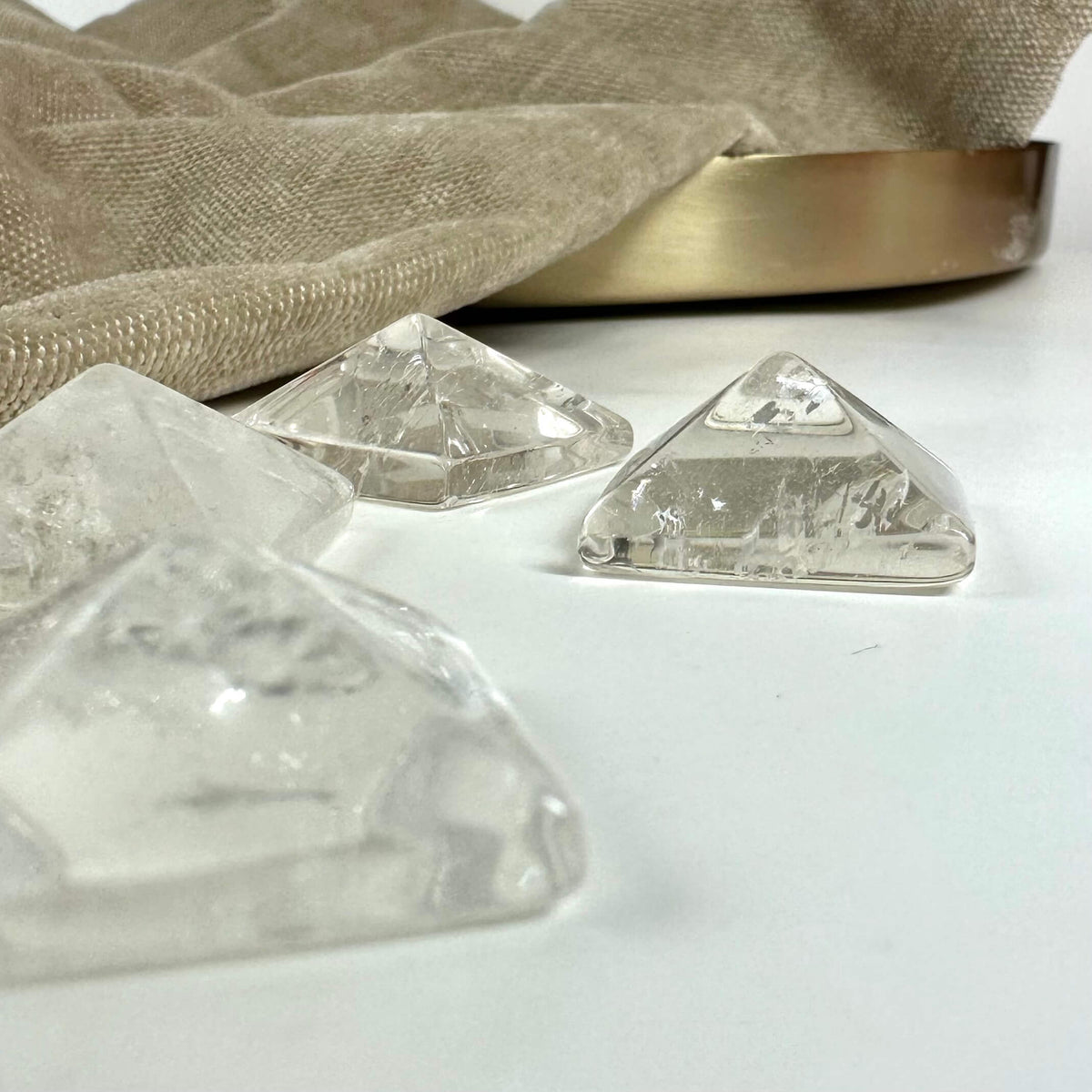 Bjergkrystal pyramider på en hvid overflade ved siden af en beige dug og guldfarvet bakke.