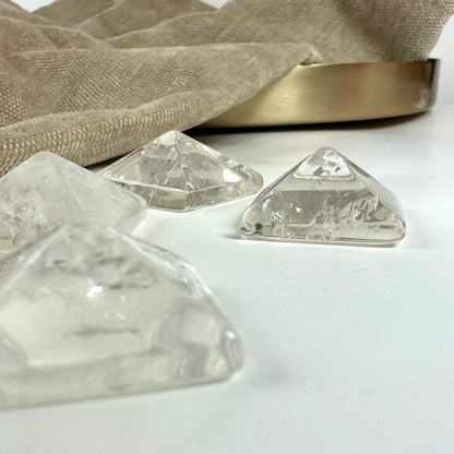 Bjergkrystal pyramider på en hvid overflade ved siden af en beige dug og guldfarvet bakke.