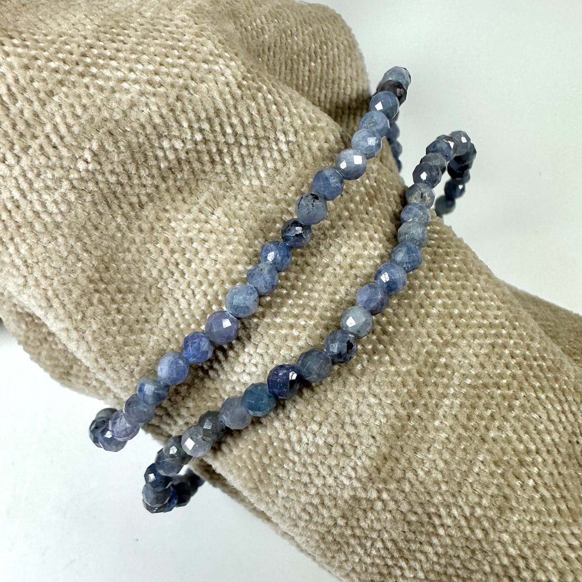 Tanzanit armbånd 4mm med facetterede perler arrangeret på en fløjlspude baggrund.