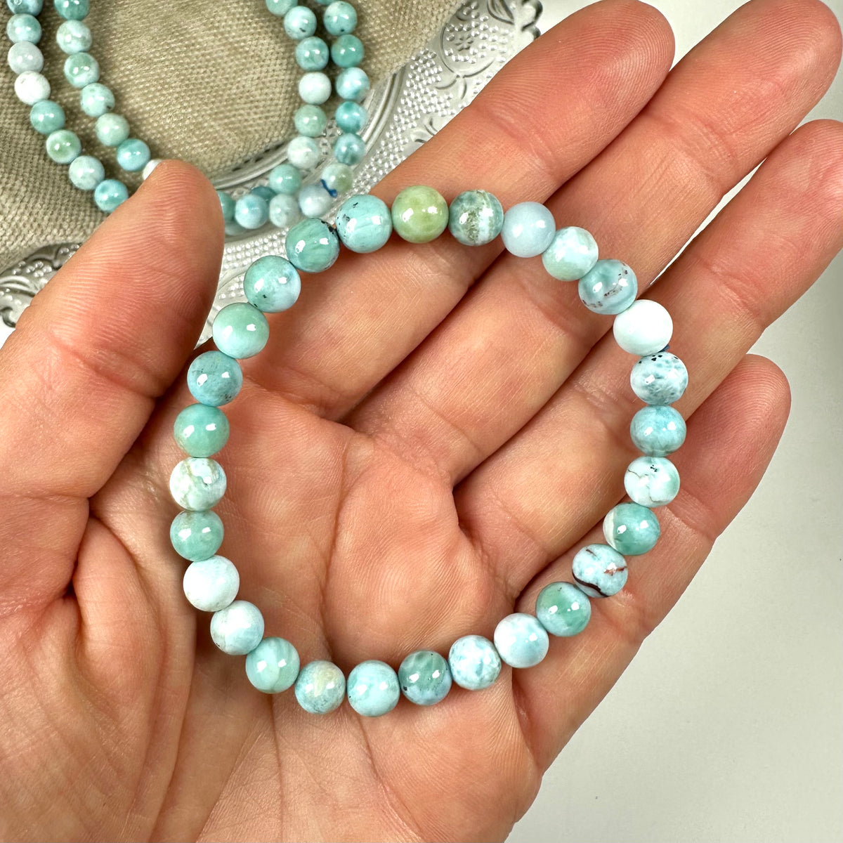 En hånd holder et 6mm Larimar armbånd med blå perler.