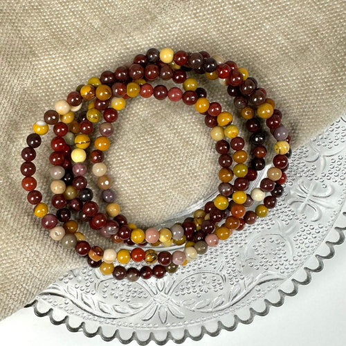 Armbånd med farverige perler på en beige tekstil- og metalbaggrund.