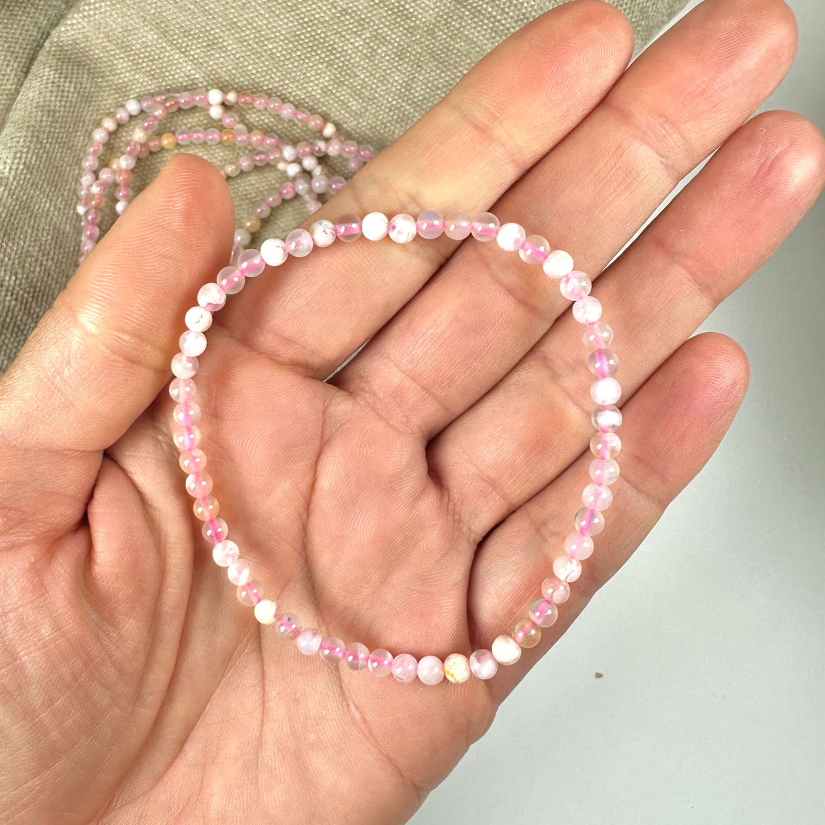 En hånd holder et Blomster Agat armbånd med små, lyserøde perler mod en neutral baggrund.