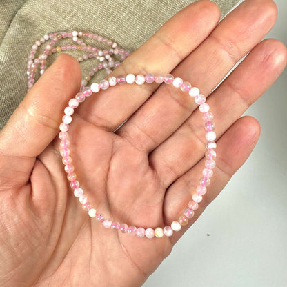 En hånd holder et Blomster Agat armbånd med små, lyserøde perler mod en neutral baggrund.