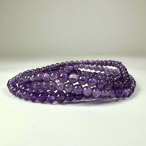 Armbånd med lilla, glatte perler lagt i en ring på en hvid baggrund.