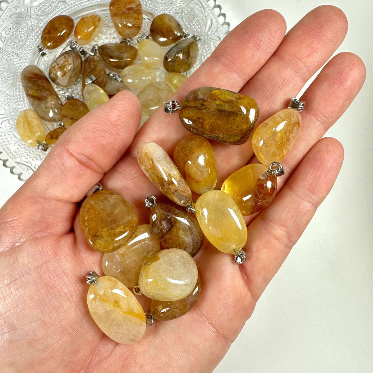 Hånd holder flere Golden healer/hæmatoid vedhæng foran tallerken med lignende sten.