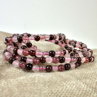 Armbånd lavet af rosa og mørke perler ligger på en beigefarvet overflade.