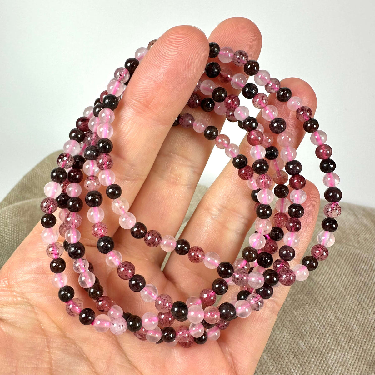 En hånd holder en halskæde af små, rosa og mørke perler på en neutral baggrund.