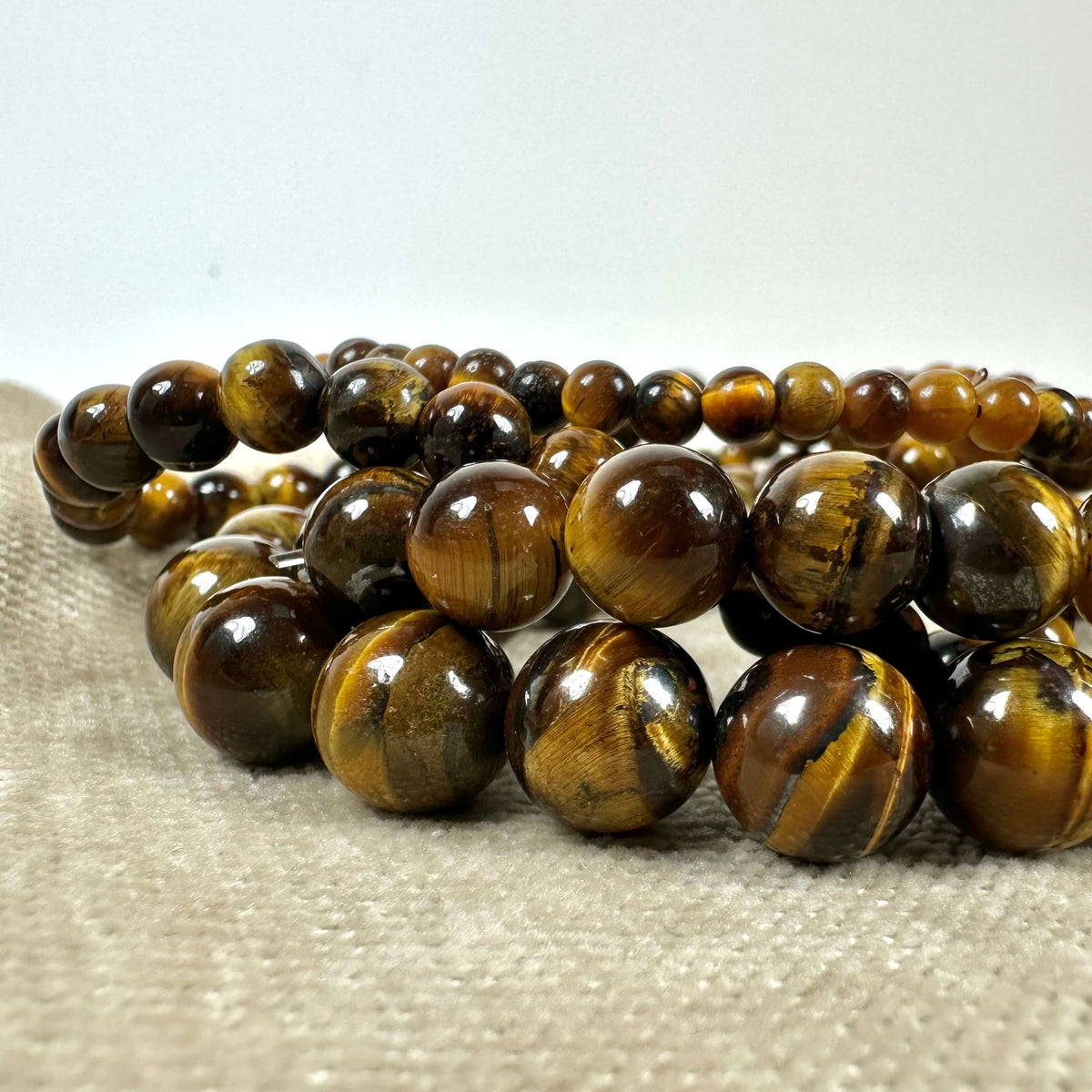 Tigerøje perlekæde ligger på en beige overflade, med glatte, brunlige stenperler i forskellige størrelser.