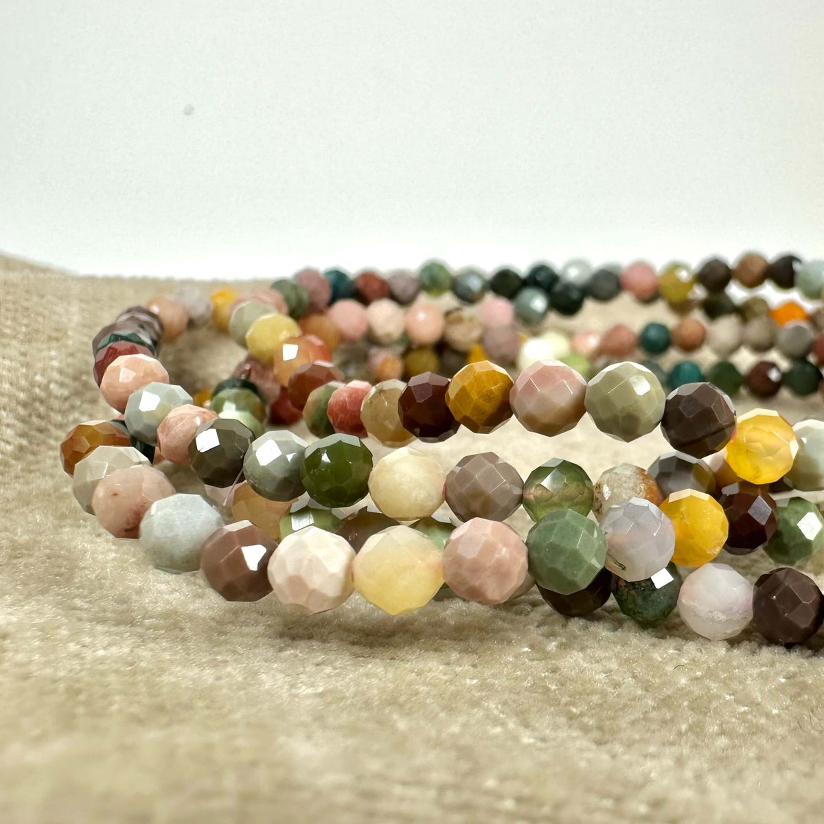 Armbånd med farverige, facetslebne sten på en beige baggrund. Stenene har nuancer af grøn, gul, brun og rosa.