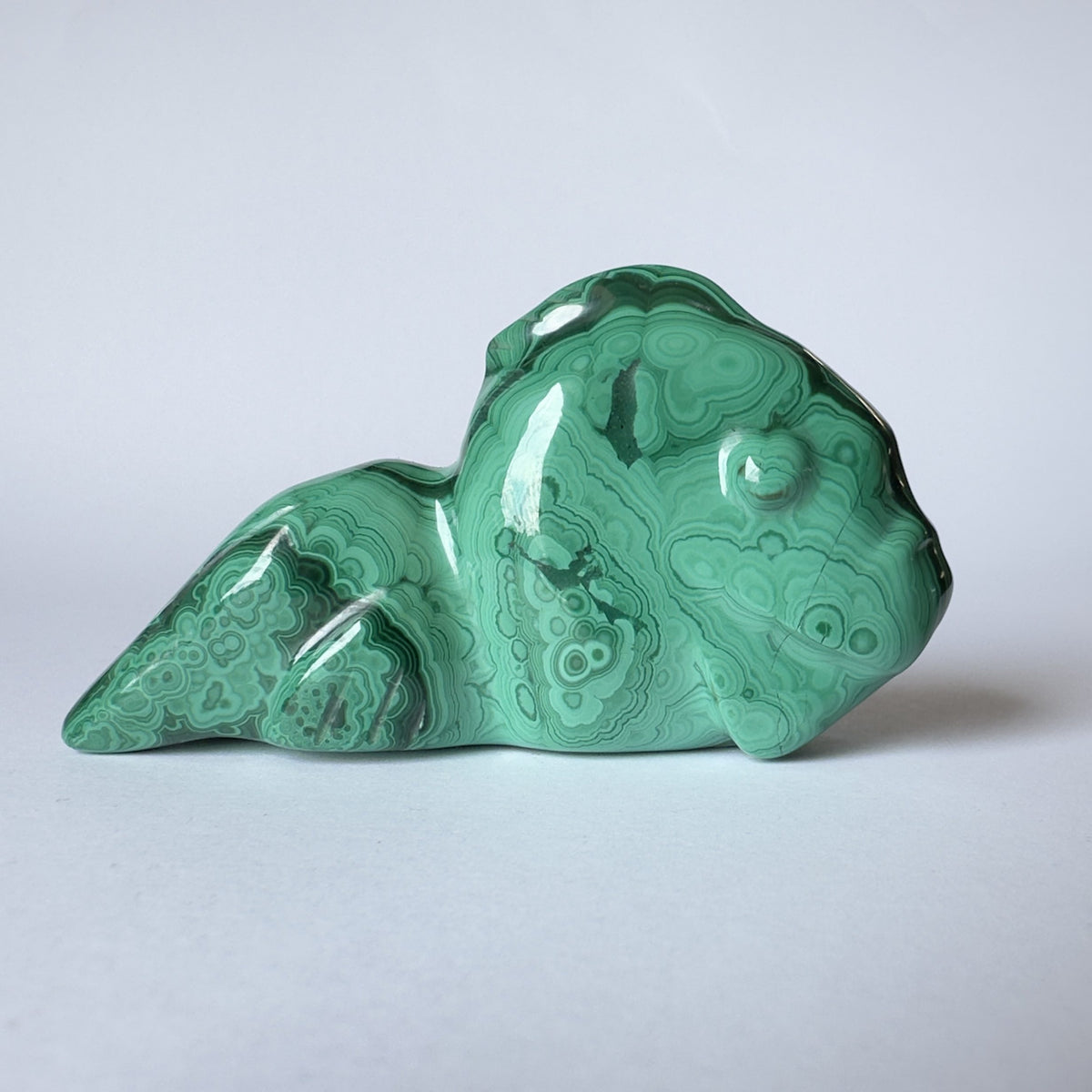 Grøn malakit skulptur formet som en slørhale på hvid baggrund.