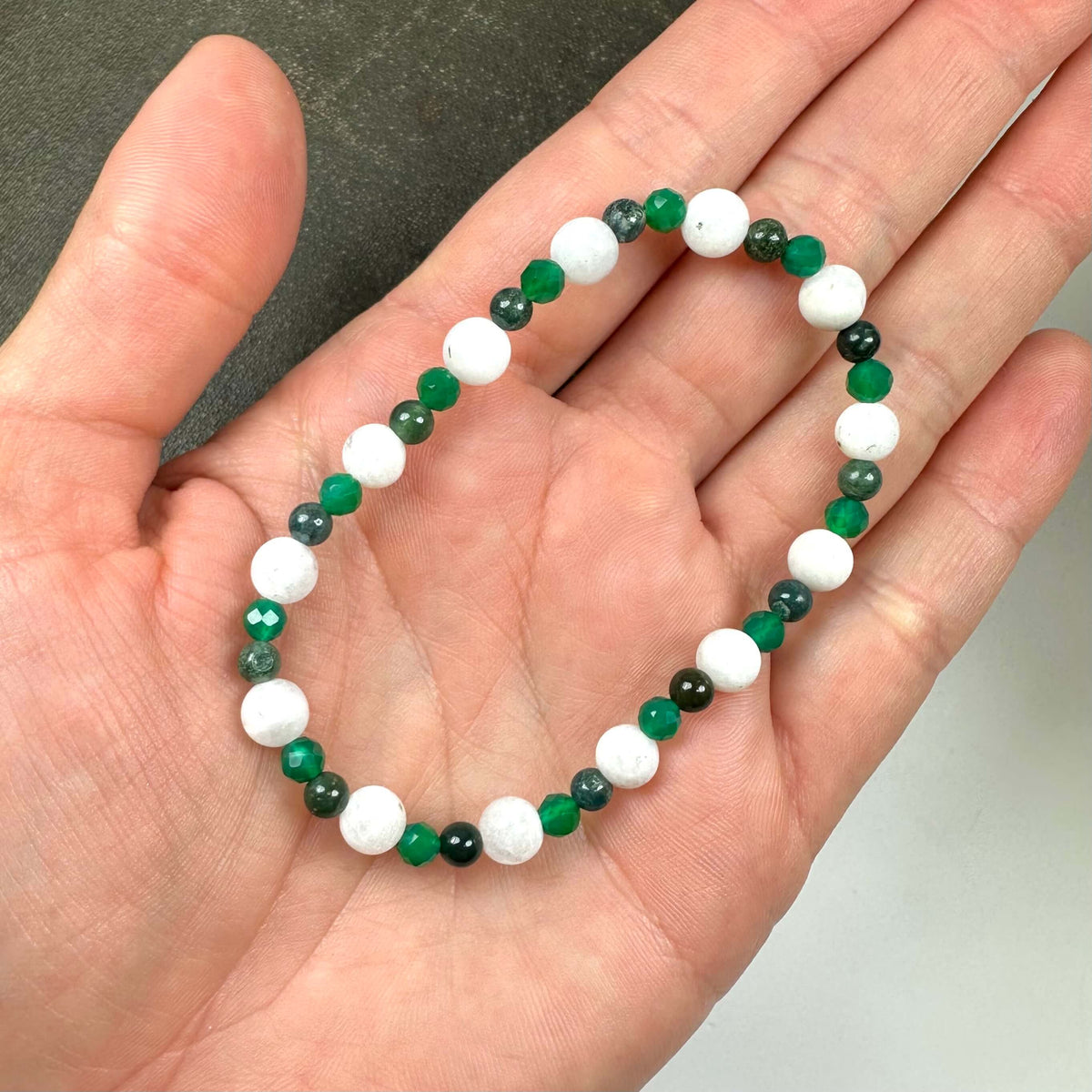 Armbånd med hvide og grønne perler i en hånd.