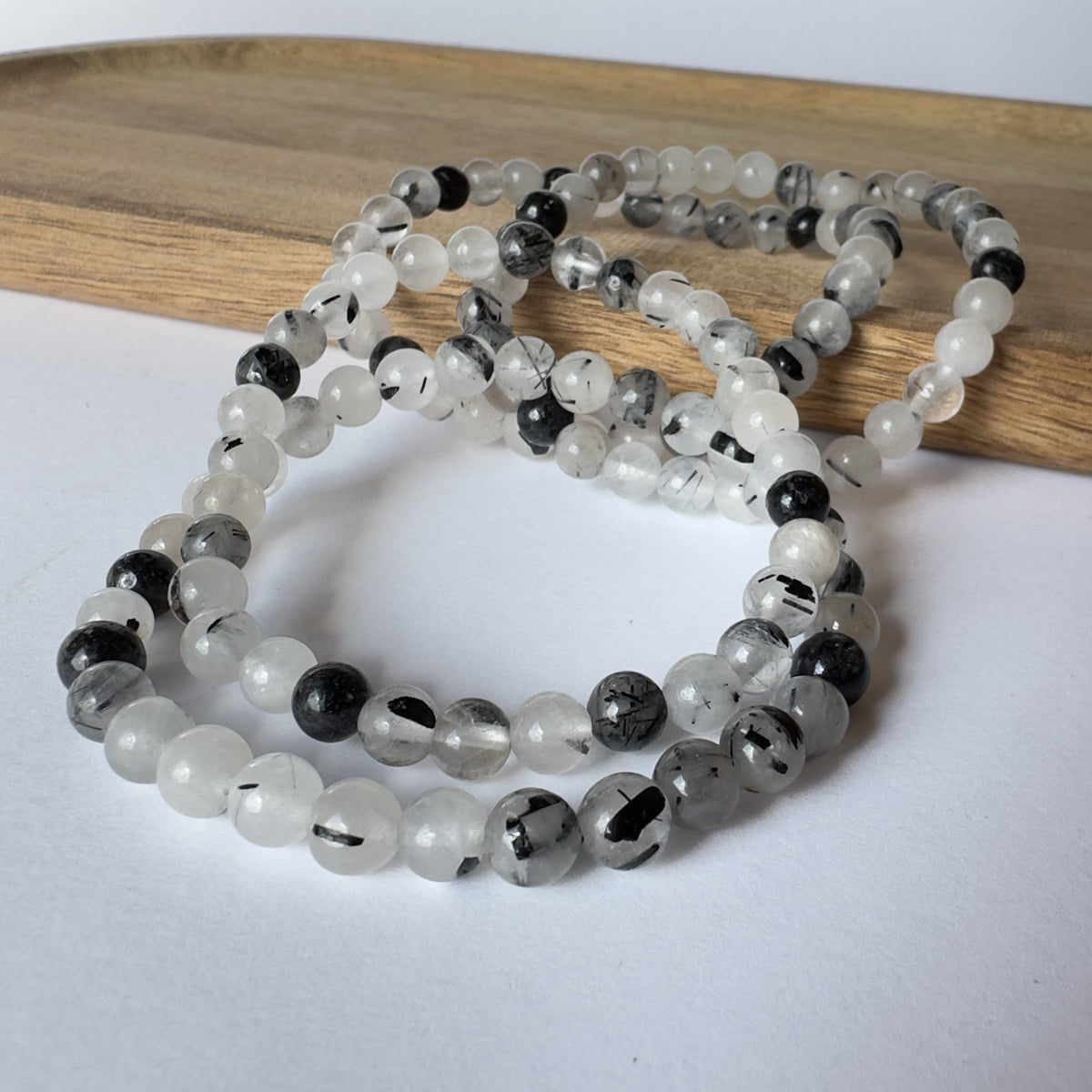 Turmalinkvarts armbånd med sorte og hvide perler, lagt på en træbakke.