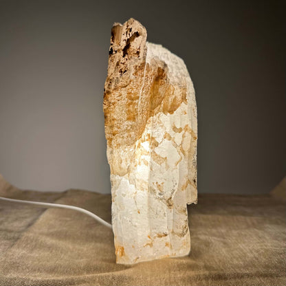 En oplyst, lys farvet stenlampe med en grov overflade på en beige baggrund.