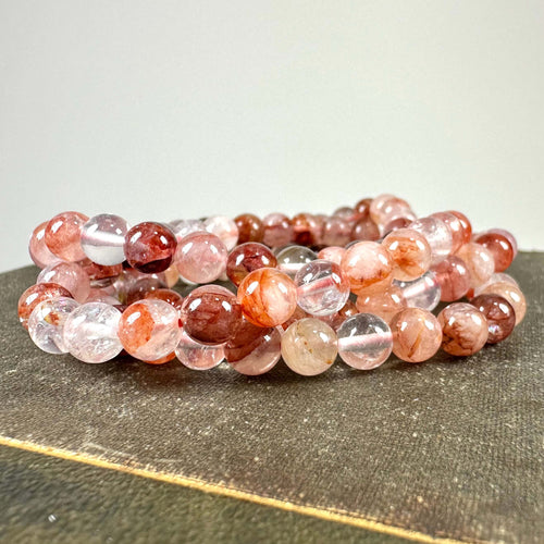 Armbånd af farverige kugler i forskellige rosa nuancer på en neutral baggrund.