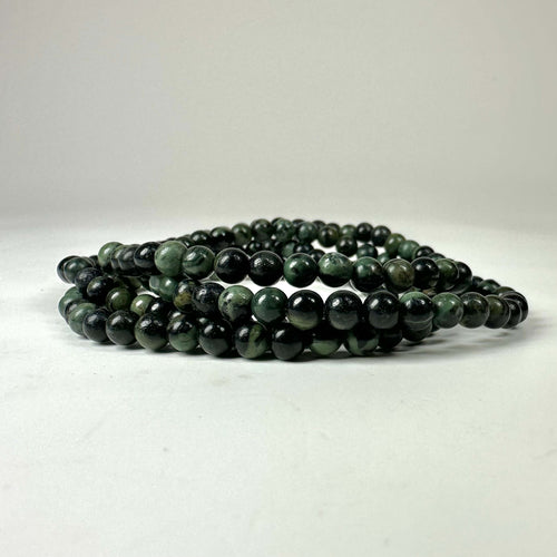Flere armbånd lavet af mørke, grønne perler på en hvid baggrund.