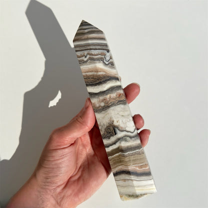 Hånd holder Zebra Calcit tårn nr. 4 med brune og hvide striber mod lys baggrund.