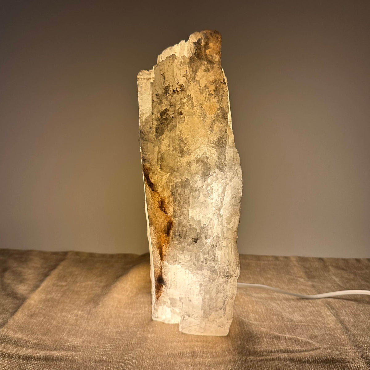 Saltlampe i stenform på bord med beige dug. Lampen lyser blødt og skaber varme nuancer i rummet.