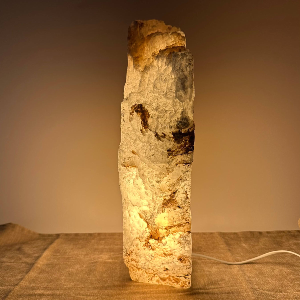 En oplyst himalayasaltlampe på et bord, der giver et varmt, hyggeligt lys mod en beige baggrund.