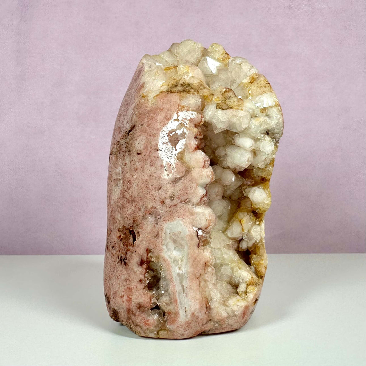 Unik pink ametystkrystal med naturlig druzy-formation står oprejst mod en blid rosa baggrund. Den sjældne sten kombinerer varme rosa nuancer med lyse, glitrende krystaller, der lyser frem fra en åben geodelomme. Pink ametyst er kendt for sin hjertehealende energi, og denne æstetisk fascinerende variant er både dekorativ og spirituelt beroligende. Velegnet til meditation og emotionel balance.