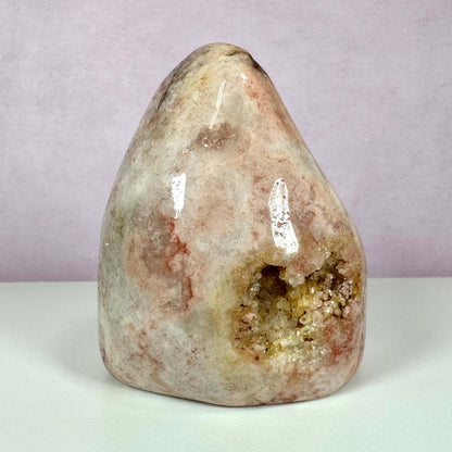 Pink Ametyst, unika – en smuk og sjælden krystal med bløde rosa nuancer og glitrende krystaller i en naturlig geodeformation. Stenen står oprejst mod en sart lyserød baggrund og fremhæver dens naturlige farvespil og polerede overflade. Den symboliserer følelsesmæssig balance og harmoni og passer perfekt til meditation og energiarbejde. Ideel til indretning og krystalsamlinger.