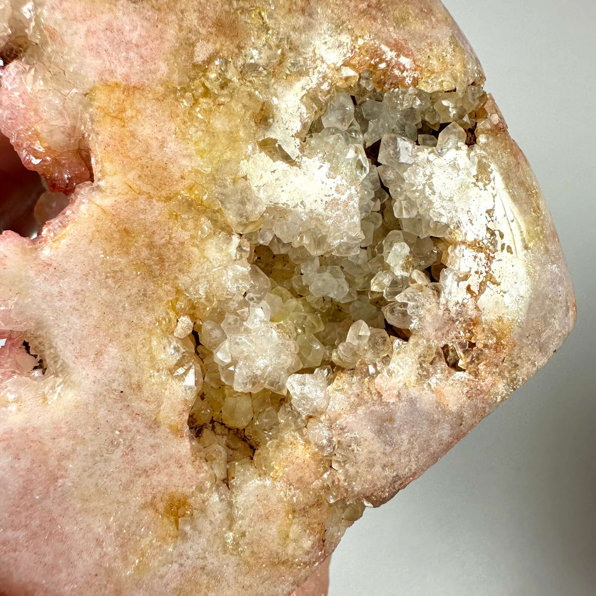 Nærbillede af en sjælden Pink Ametyst, unika, med en blanding af rosa, fersken og gyldne nuancer samt en krystallinsk druzy-overflade i midten. Krystallen er naturligt formet og fremstår rå og ubehandlet med funklende kvartskrystaller. Pink ametyst er kendt for sine healende egenskaber og forbindes med hjertchakraet, samt følelsesmæssig balance og spirituel vækst.