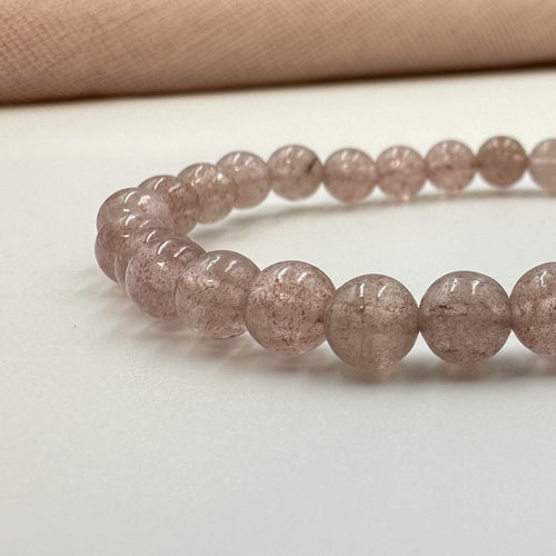 Jordbærkvarts armbånd med glatte, runde perler på lys baggrund.