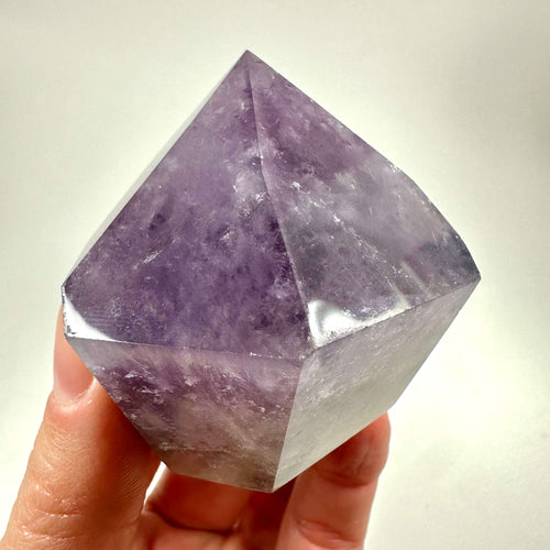 En smuk ametyst spids holdes i hånden mod en neutral baggrund og fremhæver krystallens klare, violette nuancer. Den polerede spids viser fine naturlige mønstre og struktur, karakteristisk for ametystens geologiske oprindelse. Kendt for at bringe energi, balance og spirituel indsigt, anvendes krystallen ofte til meditation og chakraarbejde. Et æstetisk og kraftfuldt værktøj fra krystilriget.com.