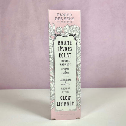 Produktet på billedet er Panier des Sens Glow Lip Balm, præsenteret i en elegant lyserød og mintgrøn æske med blomsterillustrationer. Teksten på æsken fremhæver, at læbepomaden fugter og beskytter læberne samt giver en naturlig glød. Designet understreger produktets franske oprindelse og botaniske inspiration. En læbepomade med pæonduft for bløde og strålende læber.