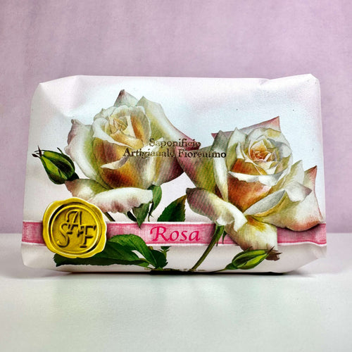 Fiorentino Rosa håndsæbe er elegant indpakket i papir med et smukt design af lyserøde og hvide roser. På forsiden ses teksten "Sapone Artigianale Fiorentino" samt et gult segl med initialerne "SAF". Den romantiske emballage udstråler italiensk luksus og klassisk charme, hvilket understreger sæbens eksklusive kvalitet. En duftende hyldest til naturlig skønhed og forkælelse af hænderne.