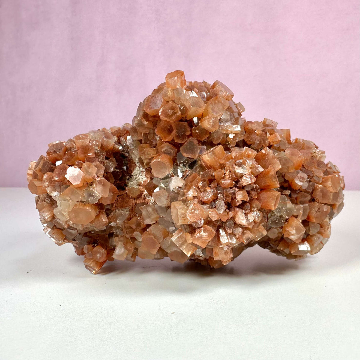 Aragonit klynge nr. 2 er en smuk, naturligt dannet krystalformation med rødbrune og gyldne nuancer, sat mod en rosa baggrund. Klyngen består af tydelige, forgrenede og spiralformede krystaller med glitrende overflader. Den udstråler ro og balance og er kendt for sine spirituelle egenskaber som jordforbindelse, stresslindring og indre stabilitet, hvilket gør den ideel til meditation og healing.
