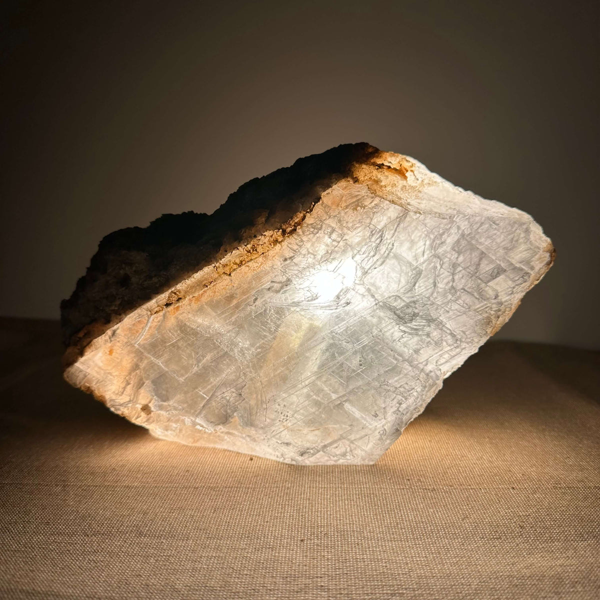 En smuk Mexicansk Selenit lampe (nr. 30) lyser blidt op og fremhæver krystallens naturlige struktur og silkebløde overflade. Lampen er håndskåret og kombinerer rustik råhed med elegant belysning. Den står på en neutral overflade og afgiver et varmt, beroligende skær, ideel til meditation, nattero eller som dekorativ energikilde i hjemmet.