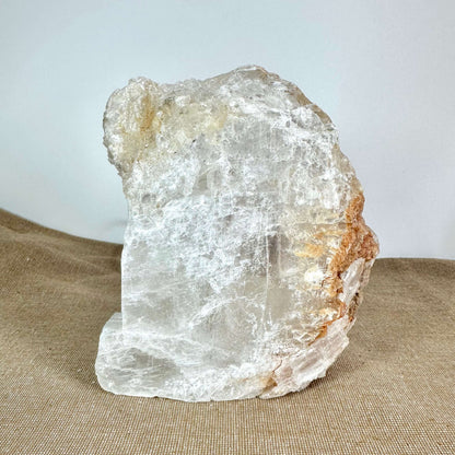 Mexicansk Selenit lampe nr. 7 er en håndlavet krystallampe skåret af naturlig selenit fra Mexico. Den har en organisk, rå form med gennemsigtig til hvid farve og naturlige strukturer. Lampen står på en lys brun overflade og har varme jordtoner i kanterne. Dens unikke krystalstruktur gør den ideel som beroligende belysning i hjemmet, perfekt til meditation, ro og velvære.