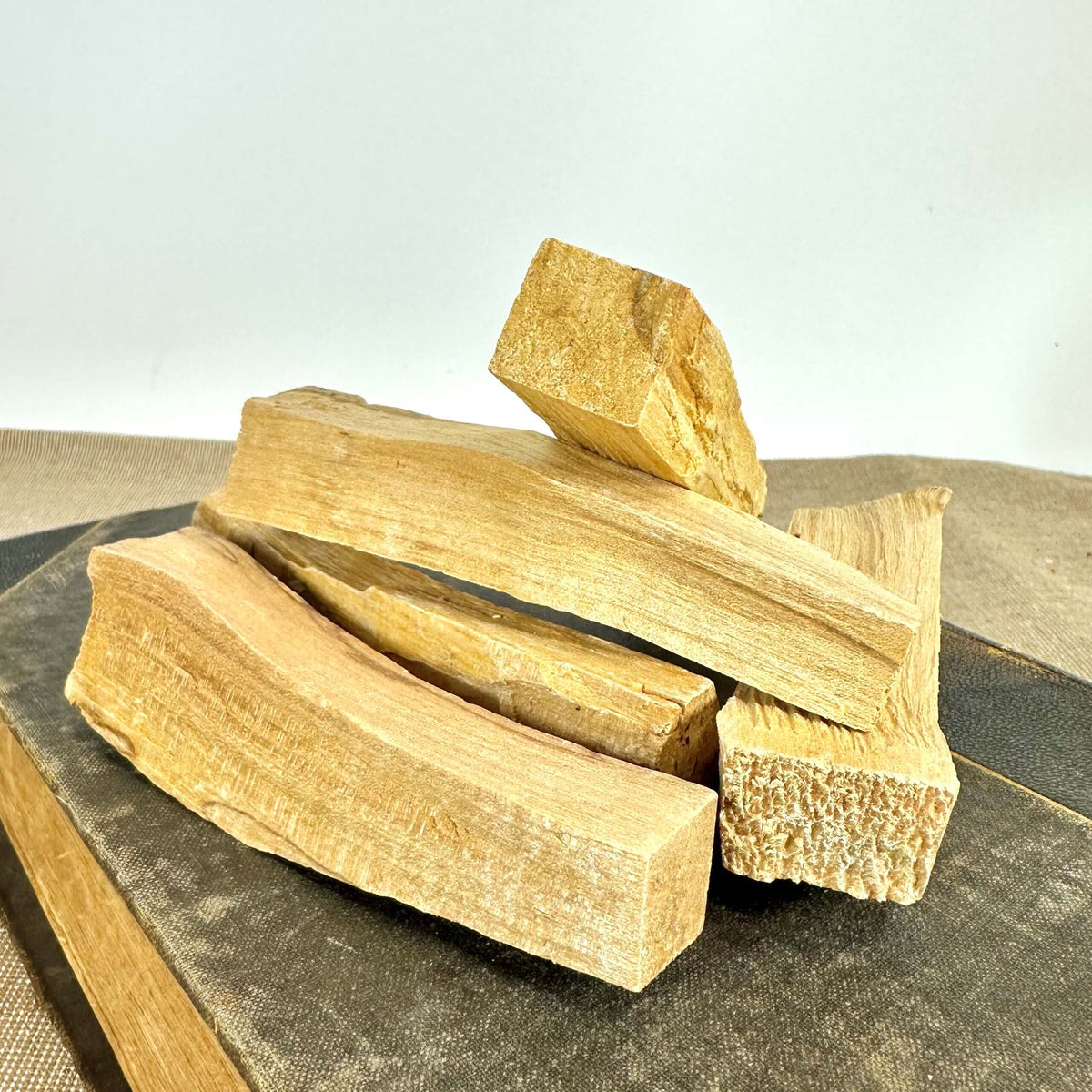 Et nærbillede af flere stykker Palo Santo stor, lagt i en dekorativ bunke på en mørk underflade. Træstykkerne har en lys gyldenbrun farve og en grov struktur. Palo Santo er kendt som et helligt træ brugt til spirituel renselse og energiarbejde. Det udsender en behagelig, aromatisk duft og bruges ofte i ceremonier og meditation for at tiltrække positiv energi.