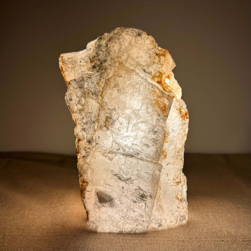 Mexicansk Selenit lampe nr. 33 lyser blidt op i varme, gyldne nuancer og fremviser sine naturlige, lagdelte krystalmønstre. Den håndskårne lampe udstråler ro og er ideel til meditation og indre balance. Selenitens silkebløde overflade og organiske form giver et æstetisk og spirituelt løft til enhver indretning og skaber en harmonisk atmosfære i rummet.