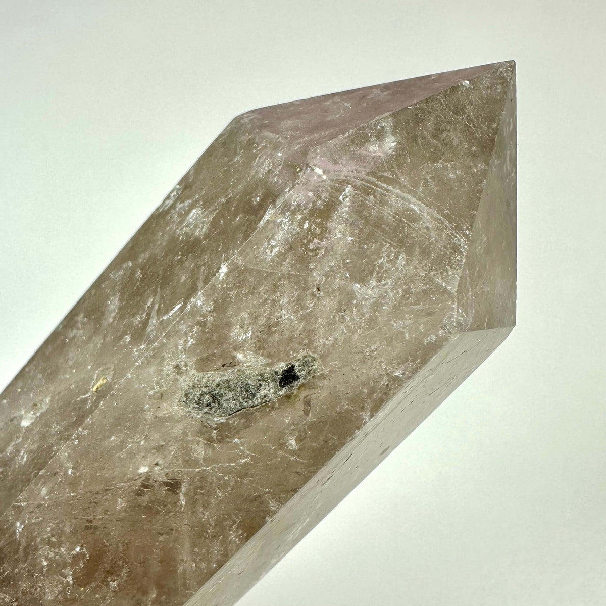 Et nærbillede af et røgkvarts tårn med en poleret, sekskantet form og spids top. Krystallen har en transparent brun til grålig farvetone med naturlige indeslutninger og ujævnheder, som tilføjer karakter. Røgkvarts er kendt for sine jordforbindende og beskyttende egenskaber og bruges ofte i meditation, energihealing og som dekoration i hjemmet eller på arbejdspladsen.