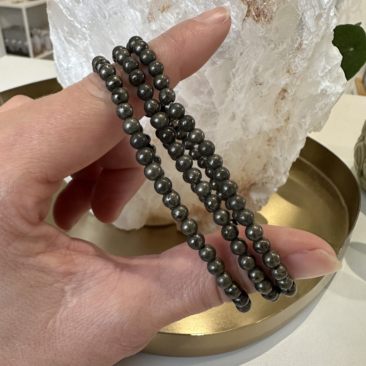 Hånd holder tre Pyrit armbånd foran en stor krystal på en gylden bakke.