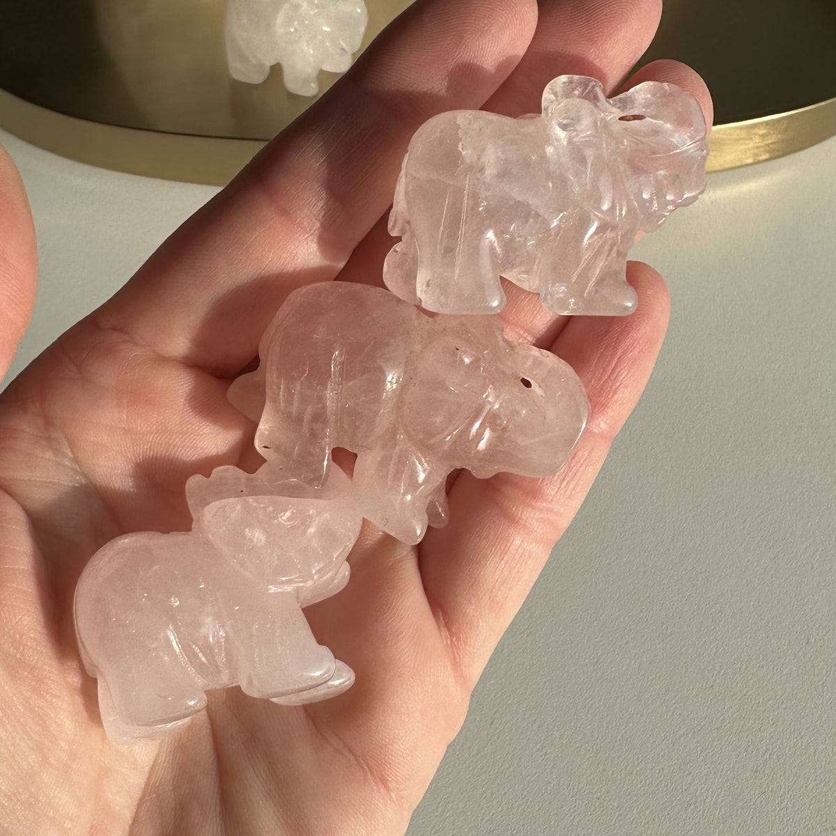 Hånd holder tre små rosenkvarts elefanter i lyserød nuance.