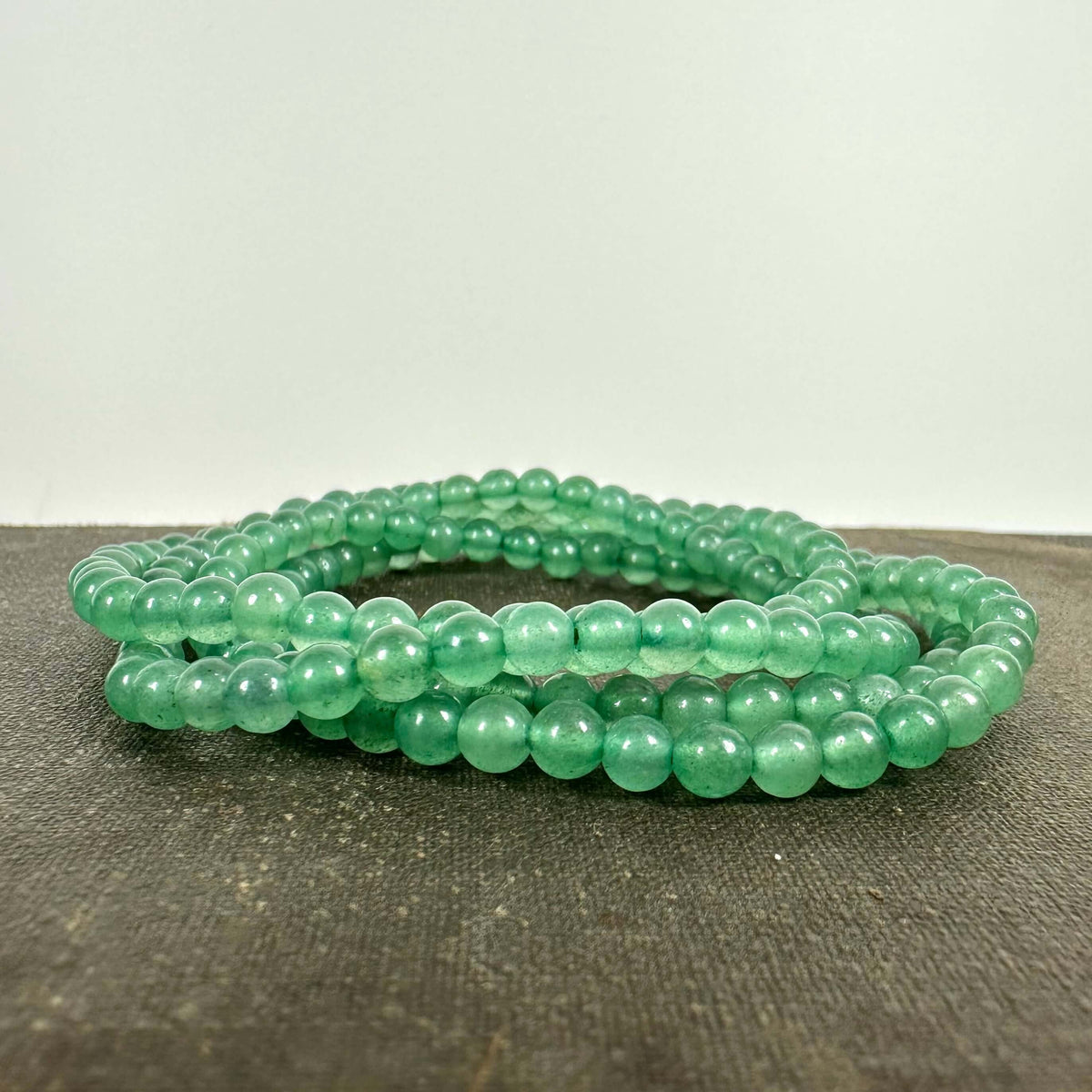 Grøn aventurin armbånd af runde, skinnende perler på en mørk overflade.