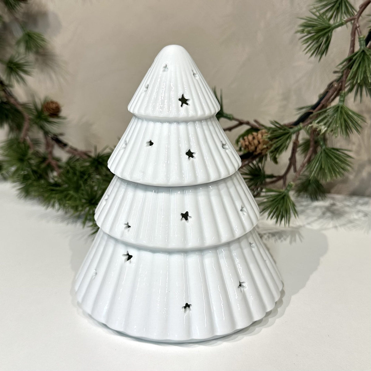 Hvid voksbrænder juletræ med stjerneformede huller, omgivet af grangrene.