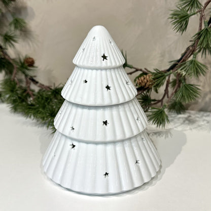 Hvid voksbrænder juletræ med stjerneformede huller, omgivet af grangrene.