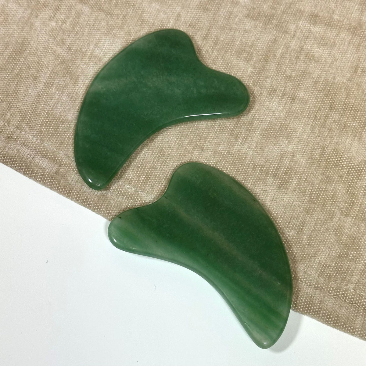 To grønne aventurin Gua Sha-sten på en stoffoverflade.