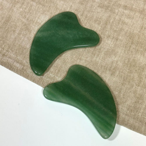 To grønne aventurin Gua Sha-sten på en stoffoverflade.