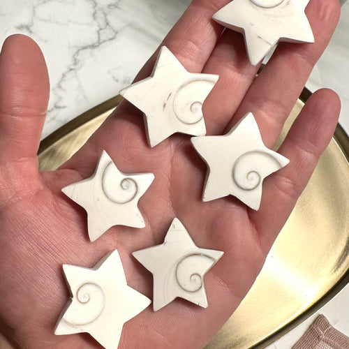Hånd med Shivas øje stjerner af hvid sten med spiraldesign. Ligger på en guldplade.